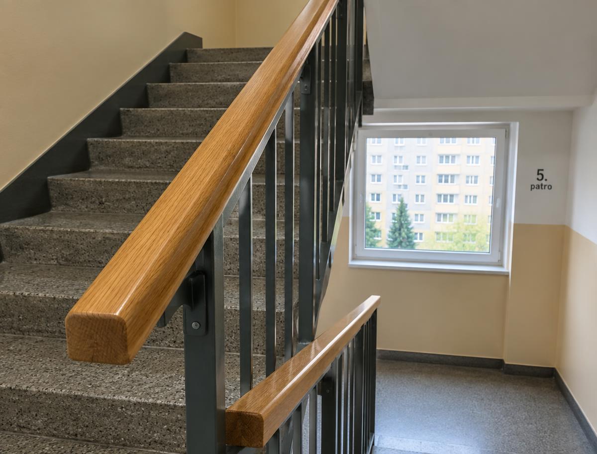 Dřevěné madlo na zábradlí ve schodišti panelového domu
